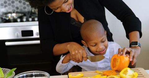 Mother Teaching Son to Chop Vegetables Together in Home Kitchen