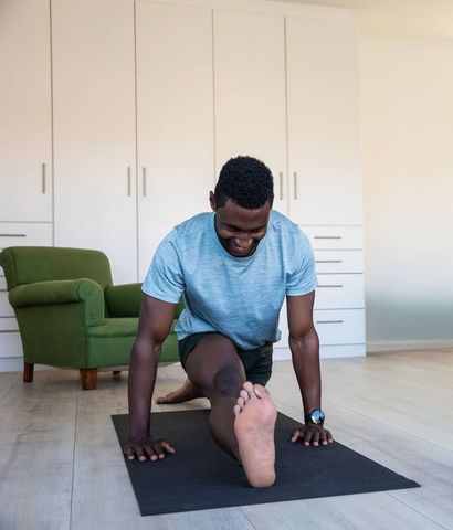 African american man performing deep lunge stretch on mat in sunlit minimalist living room