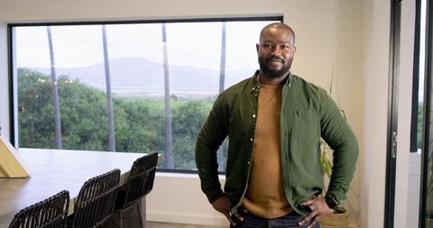 Confident African American Man Standing Hands on Hips in Sunlit Modern Home Office with Window View