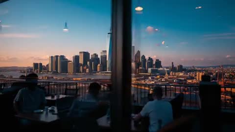 Sliding glass revealing sunset skyline over river with rooftop diners silhouetted