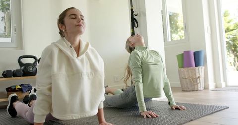Two women practicing yoga at home gym doing backbend stretch on mats in sunlit room