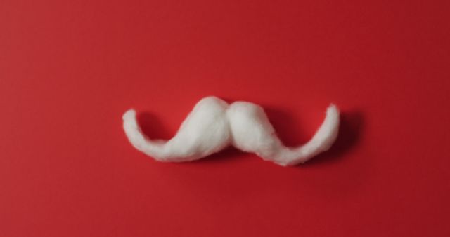 White cotton fake mustache shaped with curly ends placed on vibrant red background. Ideal for use in articles or resources about party accessories, costumes, novelty items, and decorations. Great for promoting mustache day events or moustache-themed parties.