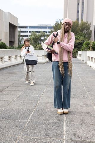 Diverse female students walking campus bridge checking smartwatch and carrying textbooks
