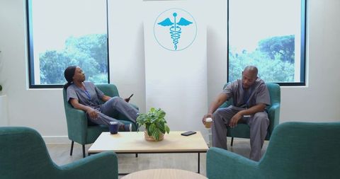 African american nurses taking break in clinic lounge with coffee and smartphones