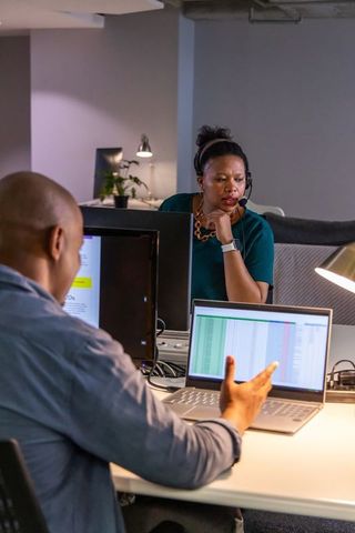 African american colleagues collaborating over spreadsheet on laptop in open-plan office