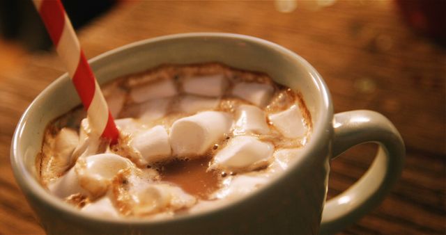 Delicious hot chocolate topped with fluffy marshmallows and served with a red striped straw in a light-colored mug suggests winter warmth and festive comfort. Ideal for use in holiday promotions, winter-themed marketing materials, food and beverage advertising, and cozy home settings.