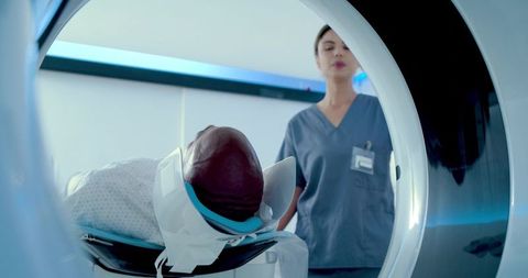 African man undergoing mri head scan with immobilizer while radiology tech monitoring procedure