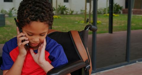 Young Boy in Wheelchair Talking on Mobile Phone in School Hallway