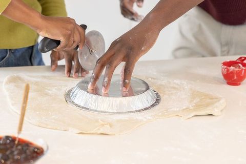 African american duo baking together cutting pie dough with pie tin and pizza cutter