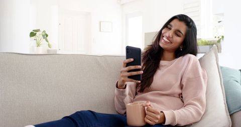 Smiling Woman Relaxing at Home With Smartphone and Coffee Mug