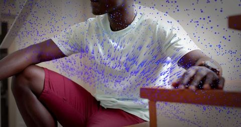 Man sitting indoors wearing wristwatch, white tee and red shorts with blue paint splatter