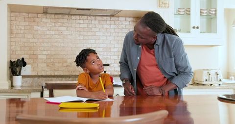 Father helping son with homework in kitchen setting