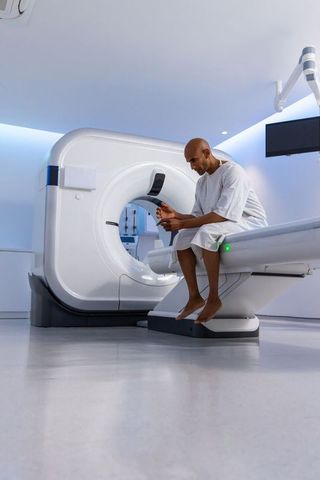 Male patient waiting on ct scanner table using smartphone in modern radiology room