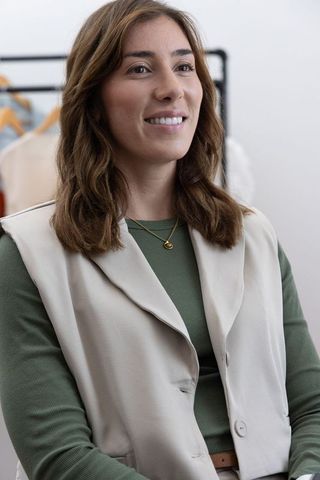 Confident woman wearing beige vest and green top smiling in boutique dressing room