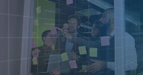 Diverse team brainstorming on glass wall with sticky notes and laptop in modern office