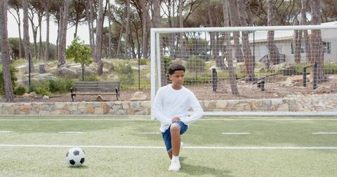 Young Boy Kneeling on Soccer Field with Ball Outdoors