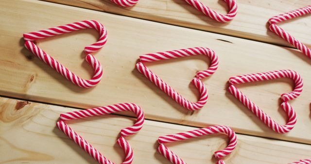 Heart-shaped red and white striped candy canes arranged in rows on wooden surface. Ideal for holiday season themes, Christmas decorations, baking projects, greeting cards, festive marketing, or social media posts. Conveys a festive and celebratory atmosphere.