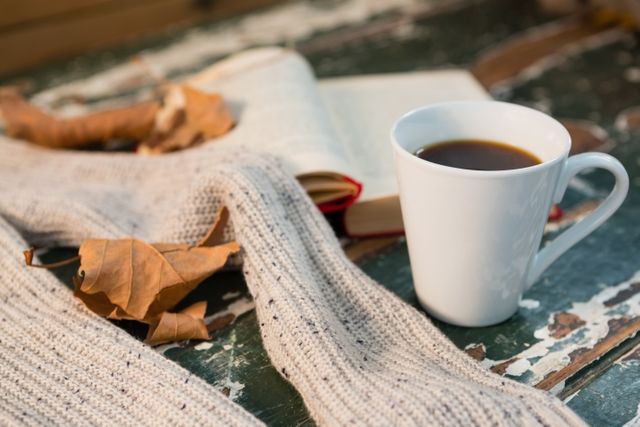 Close up of sweater by open book and coffee cup on table