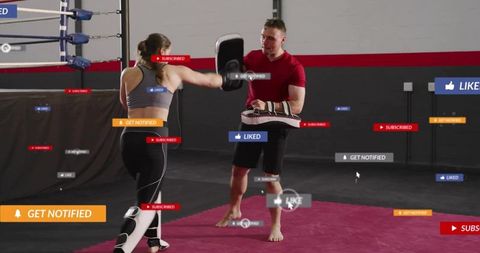 Female martial arts trainee kicking focus pads while coach holds shields in gym studio