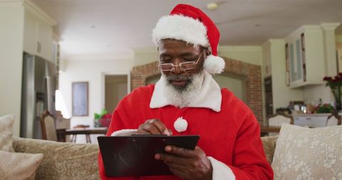 Senior man in santa claus costume with tablet at home