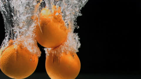 Bright Oranges Splashing into Water on Black Background