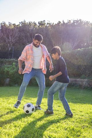 Asian father and son bonding over backyard soccer game