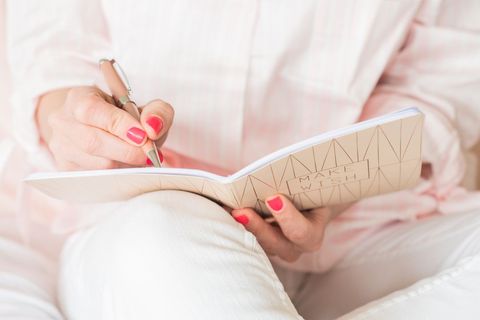 Woman writing in gold embossed notebook with pink nail polish