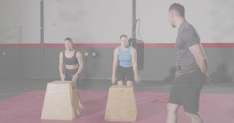 Performing box jumps under trainer supervision on red gym mat for plyometric group workout