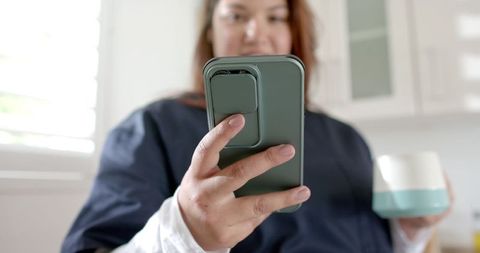 Plus size female doctor relaxing with coffee at home using smartphone