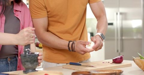 Diverse couple peeling garlic and grinding spices on kitchen counter preparing dinner