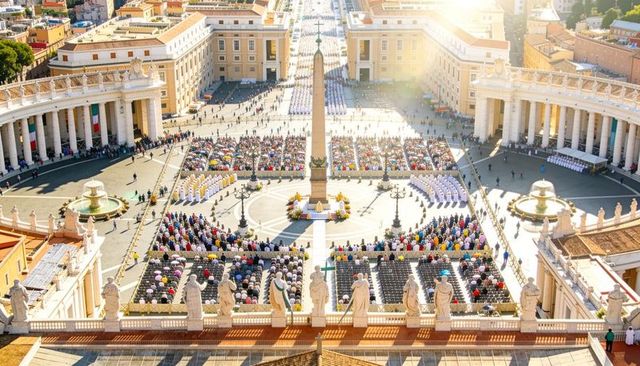 Sunlit aerial ceremony at st peter's square with central obelisk, clergy and seated worshippers