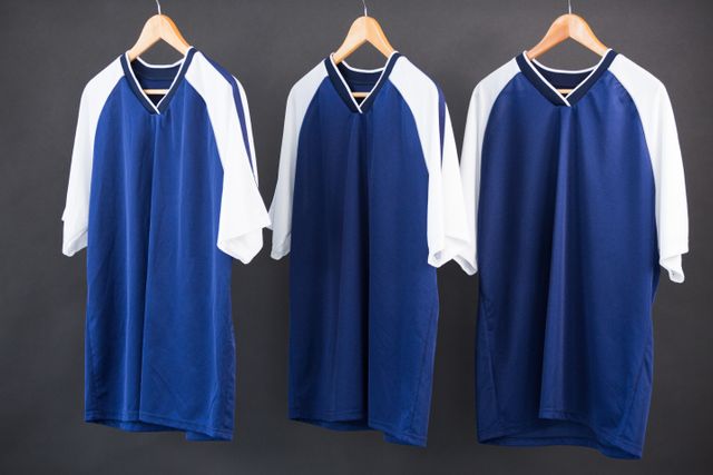 Three blue and white football jerseys hanging on wooden hangers against a black background. Ideal for use in sportswear advertisements, team uniform promotions, or athletic apparel catalogs.