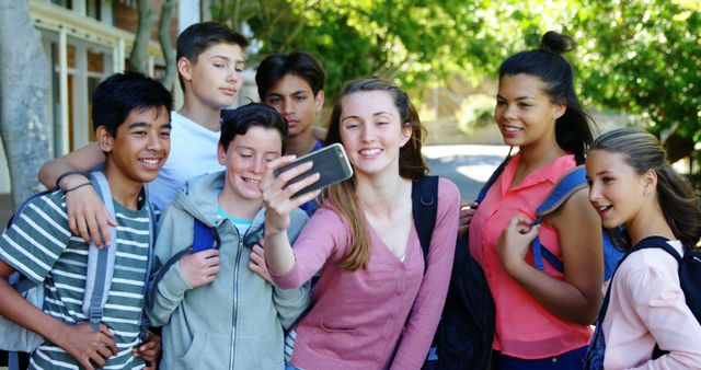 A diverse group of teenagers is gathered outdoors, smiling together as they take a selfie. They are dressed in casual clothing and have backpacks, suggesting a school or social setting. This image can be used for educational campaigns, social media content, promoting youth activities, or articles about friendship and adolescence.