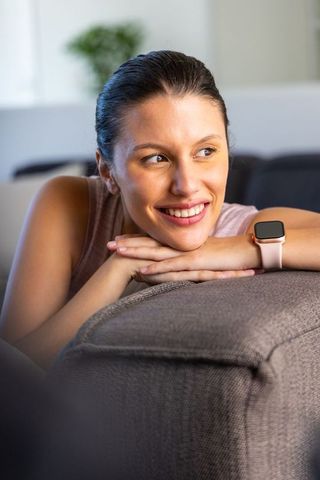 Smiling african american woman resting on sofa showing pink smartwatch band in living room