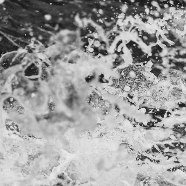 Close-up of splashing water captured in high-speed black and white photography. Water droplets creating intricate and chaotic patterns, showcasing the energy and motion of nature. Ideal for use in artistic prints, backgrounds, wall art, or anywhere a dynamic and organic abstract design is needed.