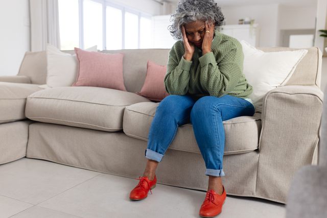 Tired, sad senior african american woman holding head, sitting in sofa living room, copy space. Retirement, senior health, inclusivity and senior lifestyle concept.