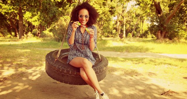 Smiling Young Woman Relaxing on Tire Swing Blowing Bubbles in Park - Download Free Stock Images Pikwizard.com