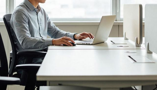 Man Working at Modern Open-Plan Office Desk Using Laptop and Mouse with Copy Space