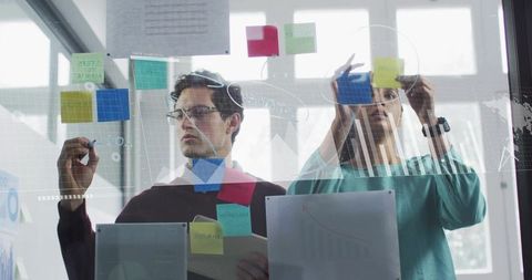 Collaborating on strategy using sticky notes on glass wall with data overlays