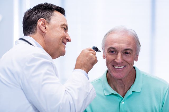Doctor examining senior patient's ear with an otoscope in a clinic. The patient is smiling, indicating a positive interaction. Useful for healthcare, medical checkups, elderly care, and professional medical services.