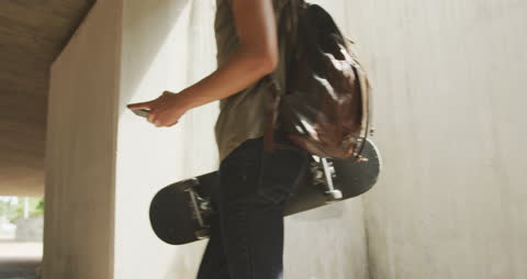 Urban Youth Walking with Backpack and Skateboard in Hand