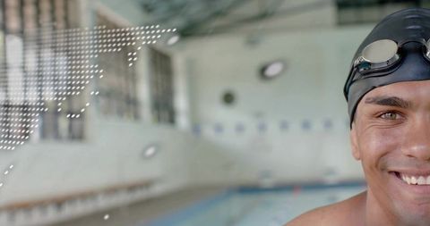 Smiling swimmer wearing black cap and goggles posing right-side at indoor pool with copy space close