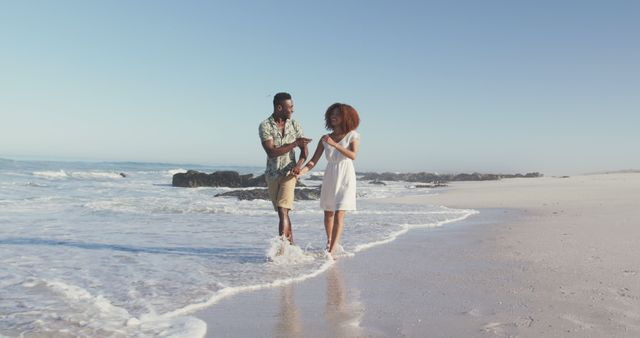 Happy diverse couple talking and walking holding hands on sunny beach in the sea. Summer, free time, relaxation, romance and vacations.