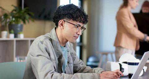 Young professional focusing on laptop in modern coworking space with coffee and greenery