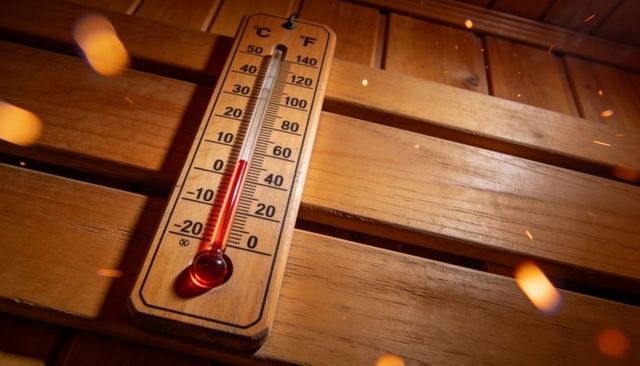 Sauna thermometer showing high heat on wooden bench with glowing embers, celsius fahrenheit scale