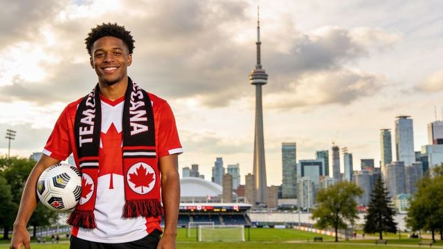 Young canadian soccer fan posing with ball and scarf against toronto cn tower skyline