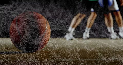 Basketball rolling releasing particle trail on shiny court with players in motion