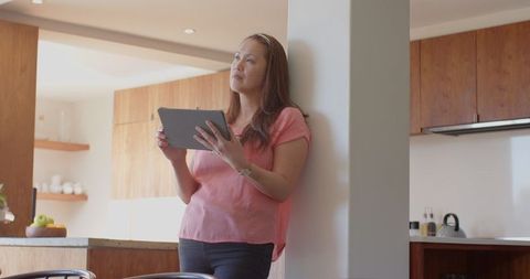 Contemplative Woman Using Tablet in Modern Kitchen