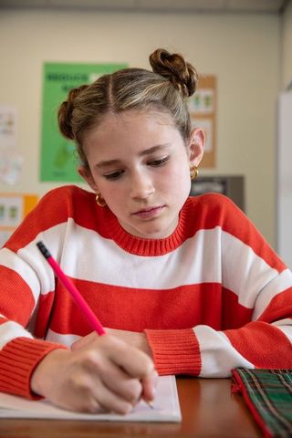 Focused schoolgirl writing in exercise book in classroom