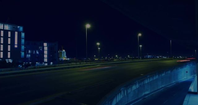 Image depicts time-lapse of vehicles moving along a well-lit street with cityscape in the background. Use for themes of urban life, transportation services, business reports and digital composites illustrating activity in metropolitan areas.